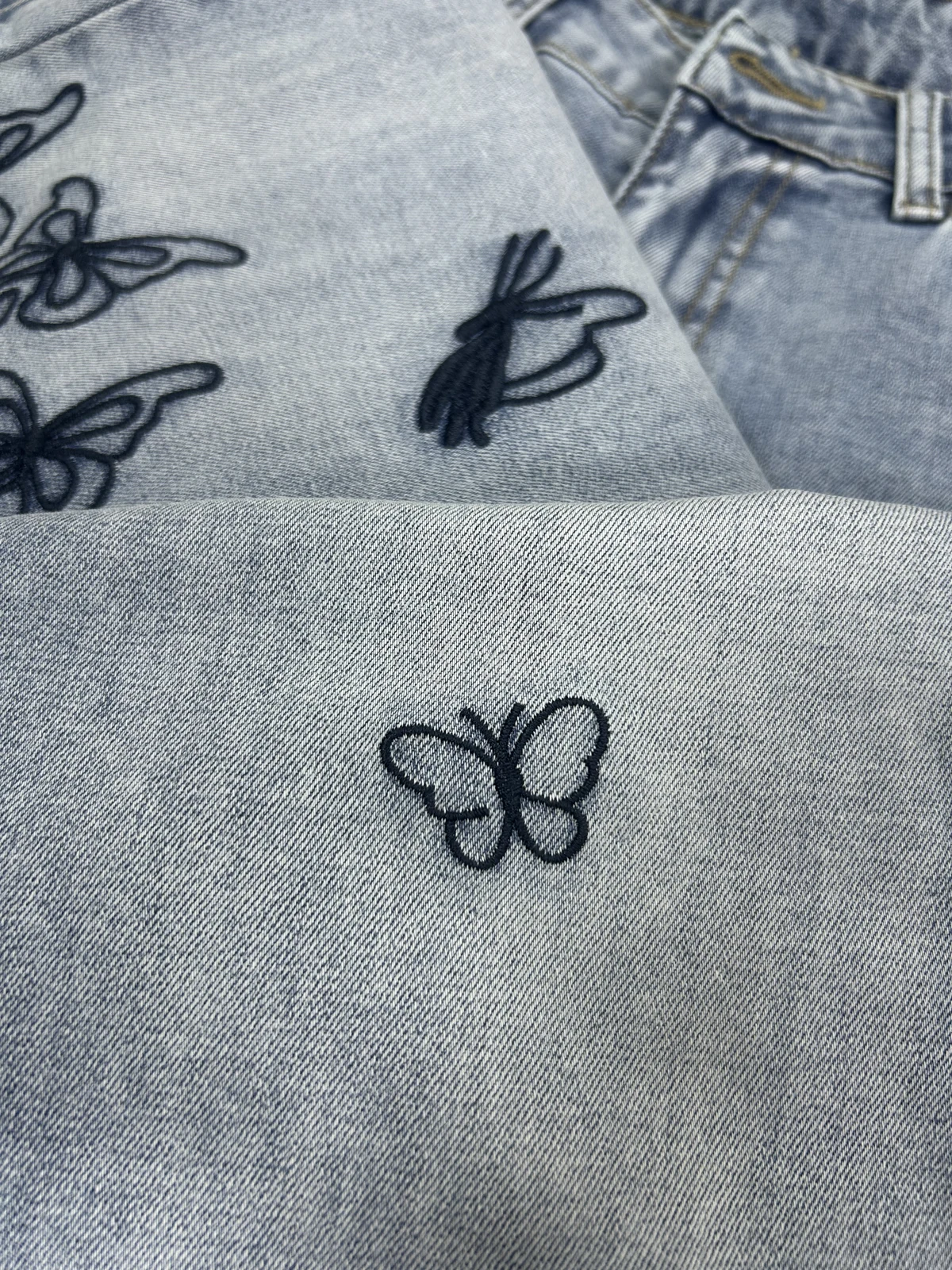 Close-up of butterfly embroidery on light wash denim