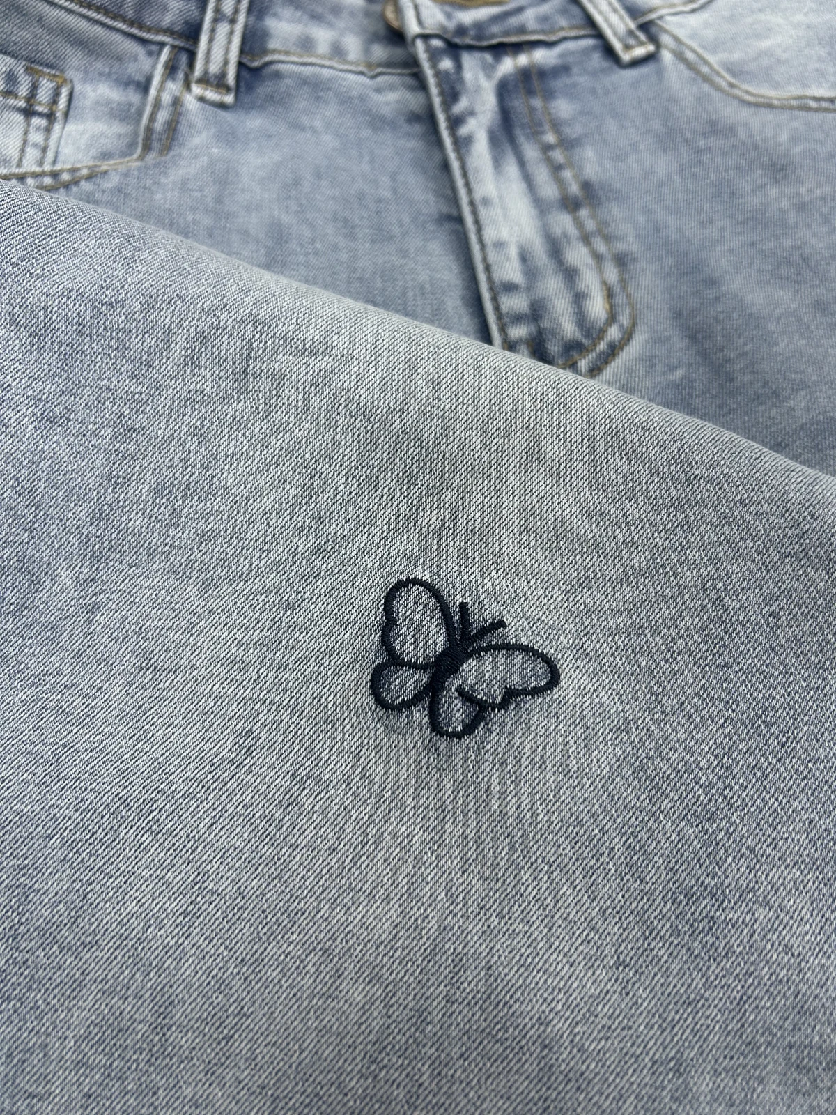 Close-up of black butterfly embroidery on light wash denim